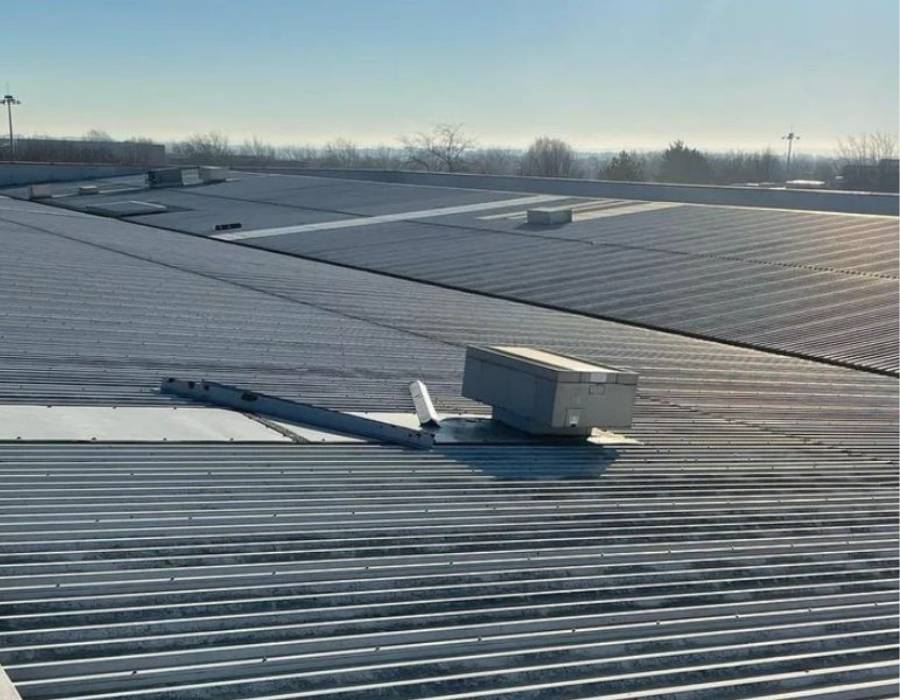 Expansive industrial metal roof with ventilation units under clear blue sky, showcasing durable roofing solutions for large-scale commercial buildings.