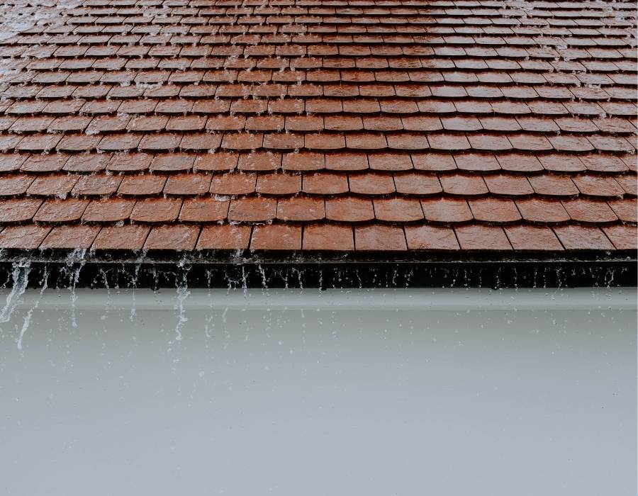 Heavy rainwater running off red shingle roof into gutters.