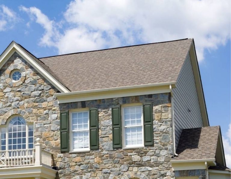 Stone exterior Maryland home with asphalt shingle roof and green shutters under blue sky.